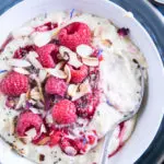 Vanillepudding-Porridge mit warmen Himbeeren in einer weißen Schüssel auf einem blauen Teller im Top View aus der Nähe mit einem Löffel, der im Haferbrei steckt und die Cremigkeit zeigt