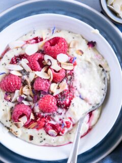 Vanillepudding-Porridge mit warmen Himbeeren in einer weißen Schüssel auf einem blauen Teller im Top View aus der Nähe mit einem Löffel, der im Haferbrei steckt und die Cremigkeit zeigt