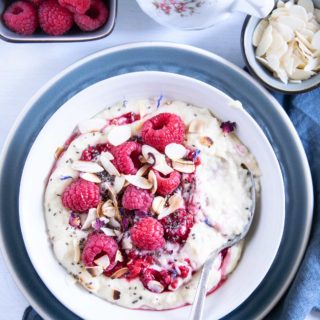 Vanillepudding-Porridge mit warmen Himbeeren in einer weißen Schüssel auf einem blauen Teller im Top View