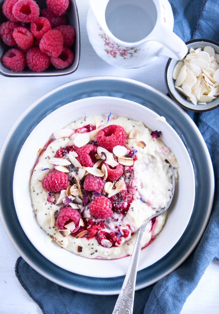 Vanillepudding-Porridge mit warmen Himbeeren in einer weißen Schüssel auf einem blauen Teller im Top View