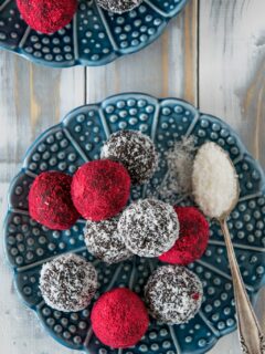 Schoko Bliss Balls mit Kokos und Himbeere auf einem blauen Teller. Aufnahmen von oben.