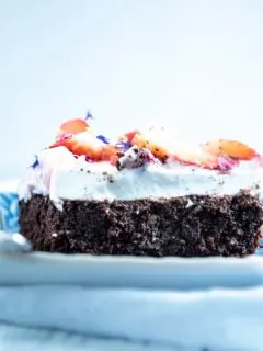 Ein Stück Brownie Style Erdbeerkuchen mit Topfen-Joghurtcreme auf einem dunkelblauen Teller mit Gabel auf Augenhöhe