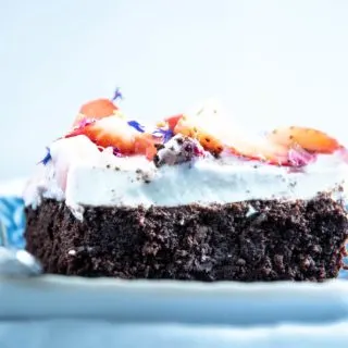 Ein Stück Brownie Style Erdbeerkuchen mit Topfen-Joghurtcreme auf einem dunkelblauen Teller mit Gabel auf Augenhöhe