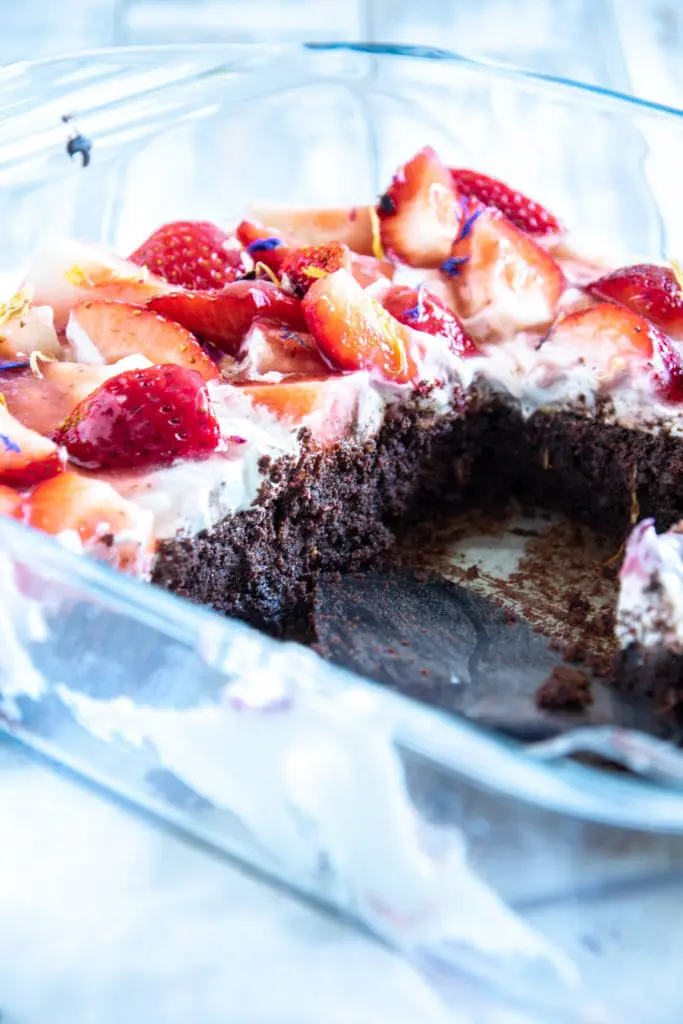 Brownie Style Erdbeerkuchen mit Topfen-Joghurtcreme in einer Glasform auf hellem Untergrund im 45-Grad-Winkel. Einige Stücke aus der Form entnommen.