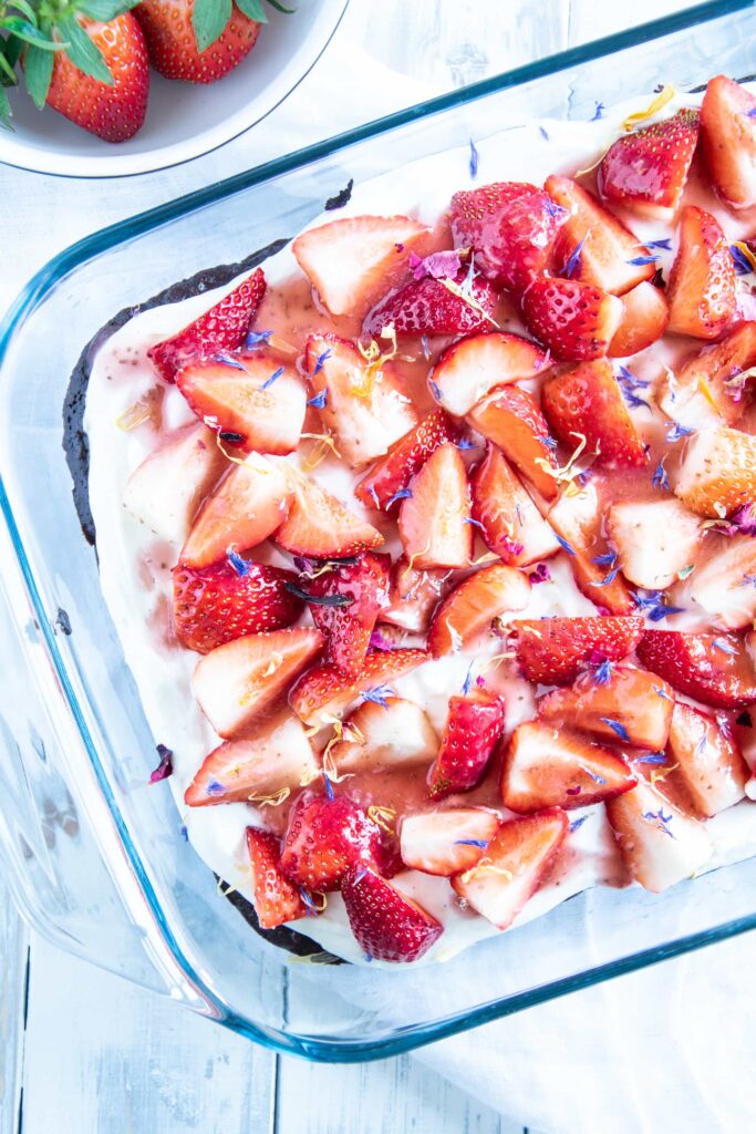 Brownie Style Erdbeerkuchen mit Topfen-Joghurtcreme in einer Glasform auf hellem Untergrund im Top View