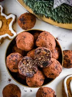 Saftige Gingerbread Energy Bites aus getrockneten Feigen, Pflaumen, Mandeln, Walnüssen, Mandelmus und Lebkuchengewürz in einer goldenen Schale mit Lebkuchen und Adventkranz als Dekoration