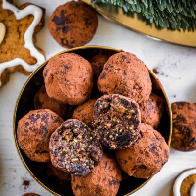 Saftige Gingerbread Energy Bites aus getrockneten Feigen, Pflaumen, Mandeln, Walnüssen, Mandelmus und Lebkuchengewürz in einer goldenen Schale mit Lebkuchen und Adventkranz als Dekoration