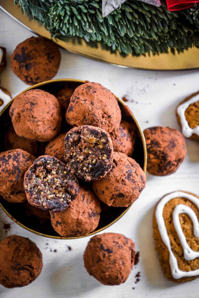 Saftige Gingerbread Energy Bites aus getrockneten Feigen, Pflaumen, Mandeln, Walnüssen, Mandelmus und Lebkuchengewürz in einer goldenen Schale mit Lebkuchen und Adventkranz als Dekoration