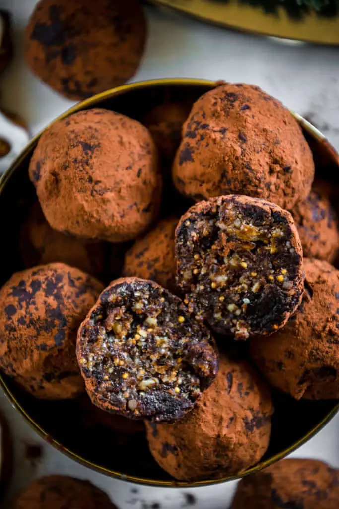 Saftige Gingerbread Energy Bites aus getrockneten Feigen, Pflaumen, Mandeln, Walnüssen, Mandelmus und Lebkuchengewürz in einer goldenen Schale mit Lebkuchen und Adventkranz als Dekoration