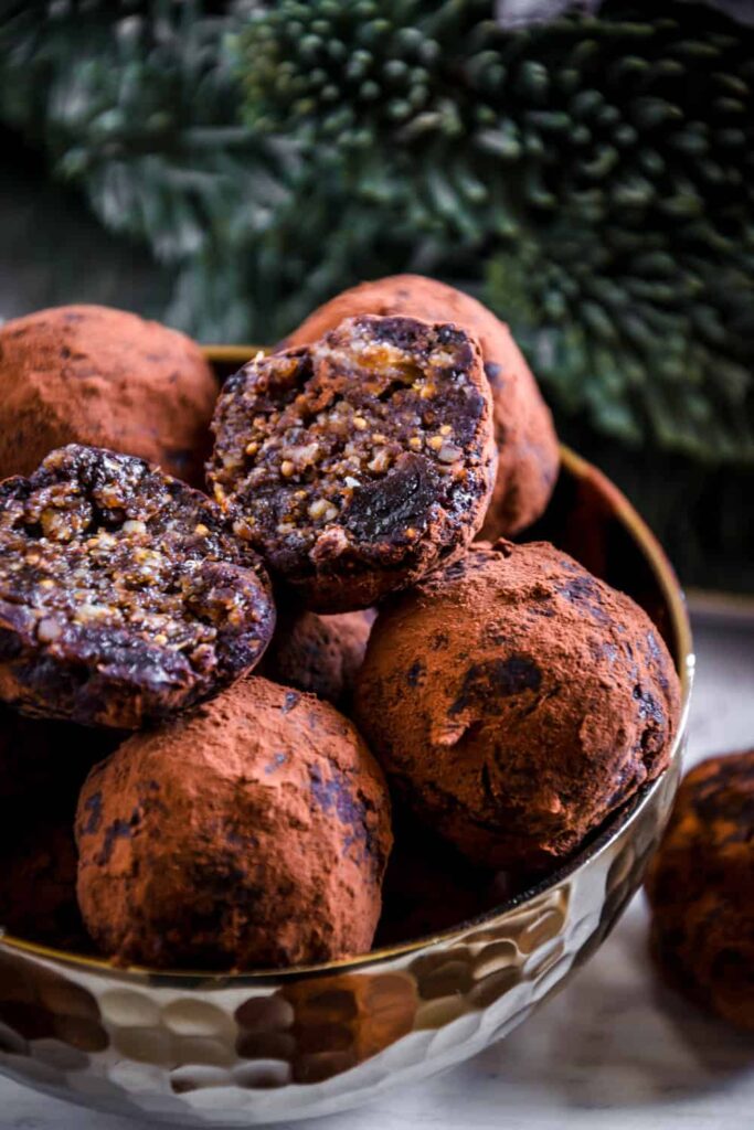 Saftige Gingerbread Energy Bites aus getrockneten Feigen, Pflaumen, Mandeln, Walnüssen, Mandelmus und Lebkuchengewürz in einer goldenen Schale mit Lebkuchen und Adventkranz als Dekoration