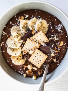 Cremiger Schokopudding-Porridge mit Schmelzflocken, Mini-Dinkelkeksen, Schokolade, gerösteten Macadamianüssen, Banane, Kokosflocken und Chiasamen