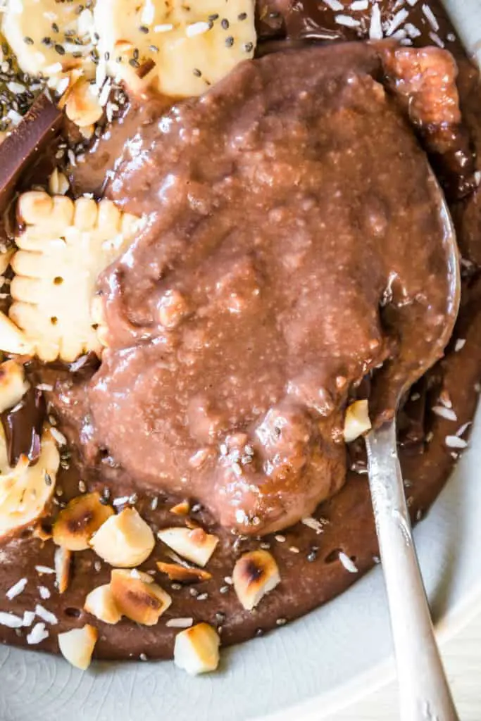 Cremiger Schokopudding-Porridge mit Schmelzflocken, Mini-Dinkelkeksen, Schokolade, gerösteten Macadamianüssen, Banane, Kokosflocken und Chiasamen