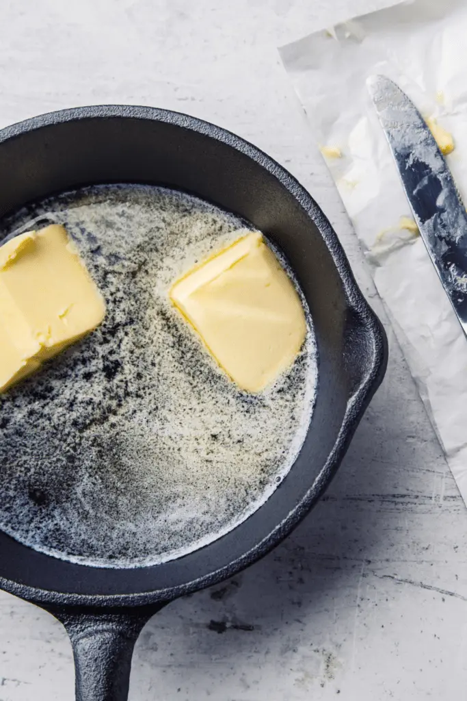 Schmelzende Butter in einer schwarzen Gusseisenpfanne auf Marmoruntergrund.