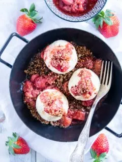 Gesunde Erdbeerknödel mit Buchweizen-Kokos-Crunch in einer schwarzen Servierpfanne mit zwei Henkeln. Heller Untergrund mit weißem Leinentuch, Gabel in der Pfanne und Erdbeeren als Deko