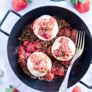 Gesunde Erdbeerknödel mit Buchweizen-Kokos-Crunch in einer schwarzen Servierpfanne mit zwei Henkeln. Heller Untergrund mit weißem Leinentuch, Gabel in der Pfanne und Erdbeeren als Deko