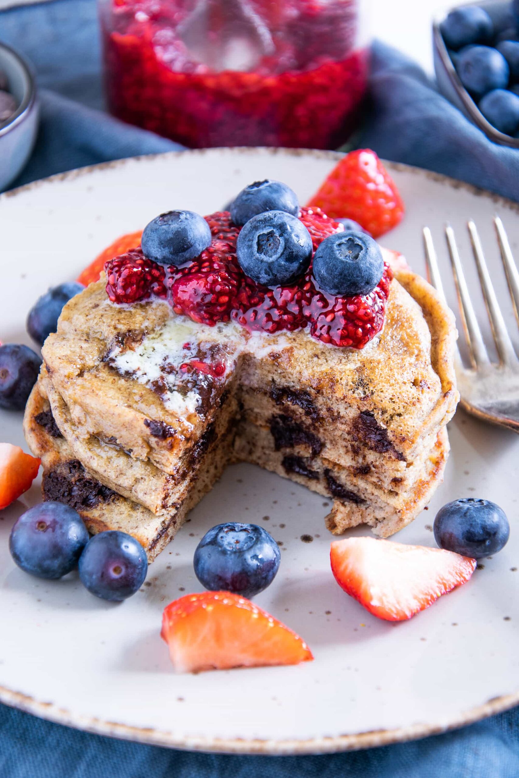 Ein Stapel Keto Chocolate Chip Pancakes, aus dem ein Viertel herausgeschnitten ist, sodass man die weiche Textur und die geschmolzenen Schokolade sehen kann. Aufnahme im 45°-Winkel.