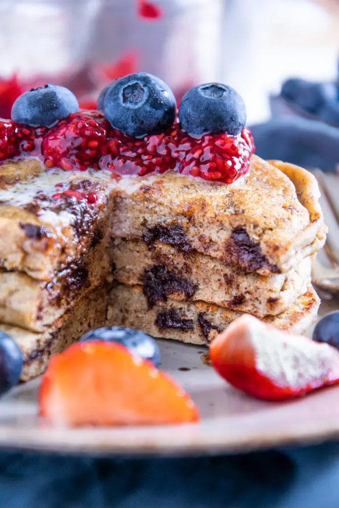 Ein Stapel Keto Chocolate Chip Pancakes, aus dem ein Viertel herausgeschnitten ist, sodass man die weiche Textur und die geschmolzenen Schokolade sehen kann. Aufnahme im 45°-Winkel.