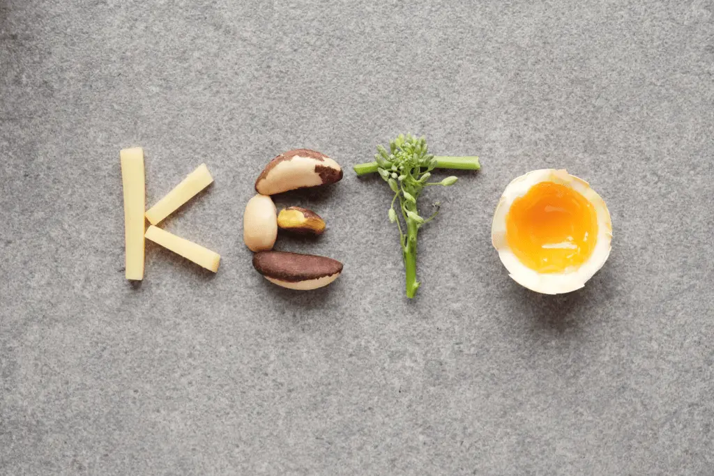 Das Wort "Keto" geschrieben mit ketogenen Lebensmitteln: Käse, Paranusskerne, grünes Gemüse und Ei.