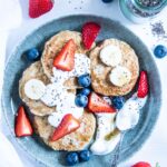 Hafer-Power-Pancakes in einem Bogen auf einem türkisen Teller angerichtet. Getoppt mit Joghurt, Beeren, Bananenscheiben und Chiasamen. Top View.