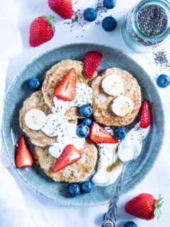 Hafer-Power-Pancakes in einem Bogen auf einem türkisen Teller angerichtet. Getoppt mit Joghurt, Beeren, Bananenscheiben und Chiasamen. Top View.