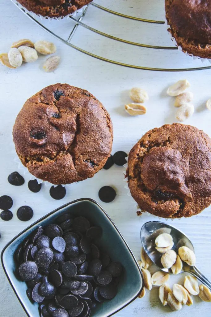 Peanut Chocolate Chip Muffins auf weißem Untergrund mit einer Schüssel Chocolate Chips und einem Teelöffel mit Erdnüssen. Top View.