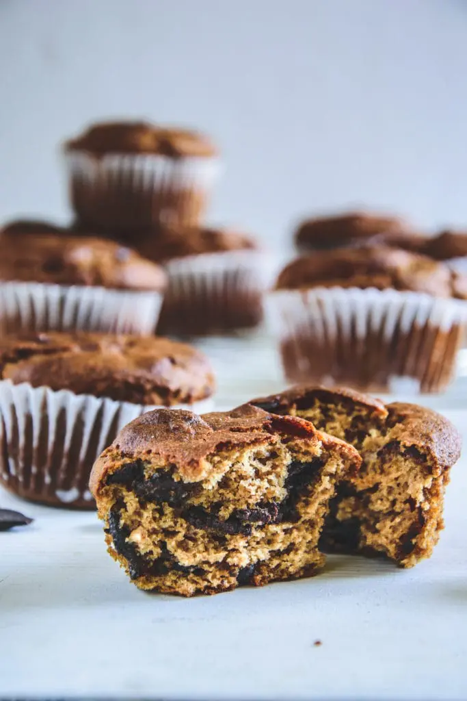 Ein halbierter Peanut Chocolate Chip Muffins mit der Textur im Fokus und weiteren Muffins im Hintergrund. Fotografiert auf Augenhöhe.
