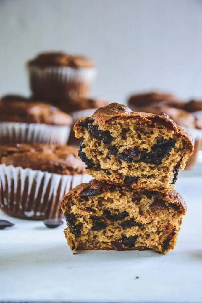 Ein halbierter Peanut Chocolate Chip Muffins mit der Textur im Fokus und weiteren Muffins im Hintergrund. Fotografiert auf Augenhöhe.