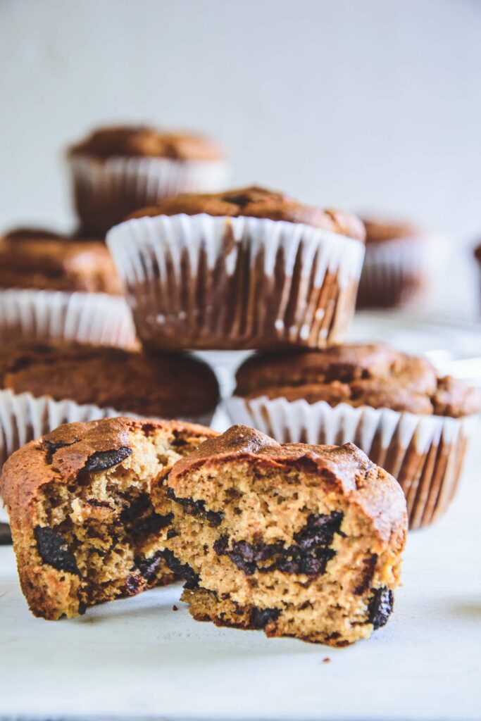 Ein halbierter Peanut Chocolate Chip Muffins mit der Textur im Fokus und weiteren Muffins im Hintergrund. Fotografiert auf Augenhöhe.