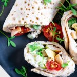 Power Wraps mit Avocado, Hüttenkäse und Kichererbsen, garniert mit Kresse. Aufgeschnitten auf einem schwarzen Teller.