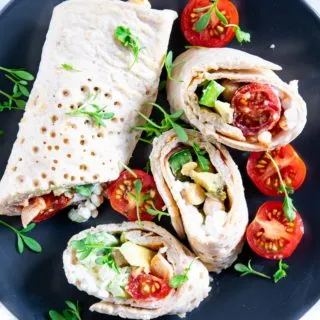 Power Wraps mit Avocado, Hüttenkäse und Kichererbsen, garniert mit Kresse. Aufgeschnitten auf einem schwarzen Teller.