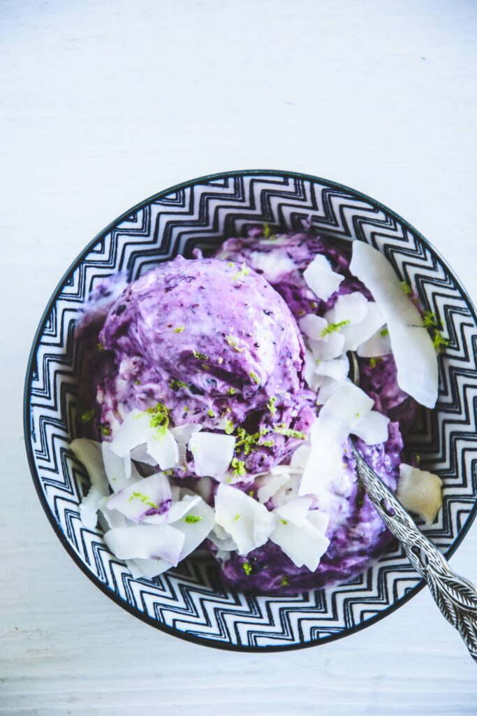 Frozen Blueberry Skyr garniert mit Kokoschips und abgeriebener Limettenschale in einer dunkelblau-weiß gemusterten Schüssel. Löffel mit kunstvollem Stiel. Top View.