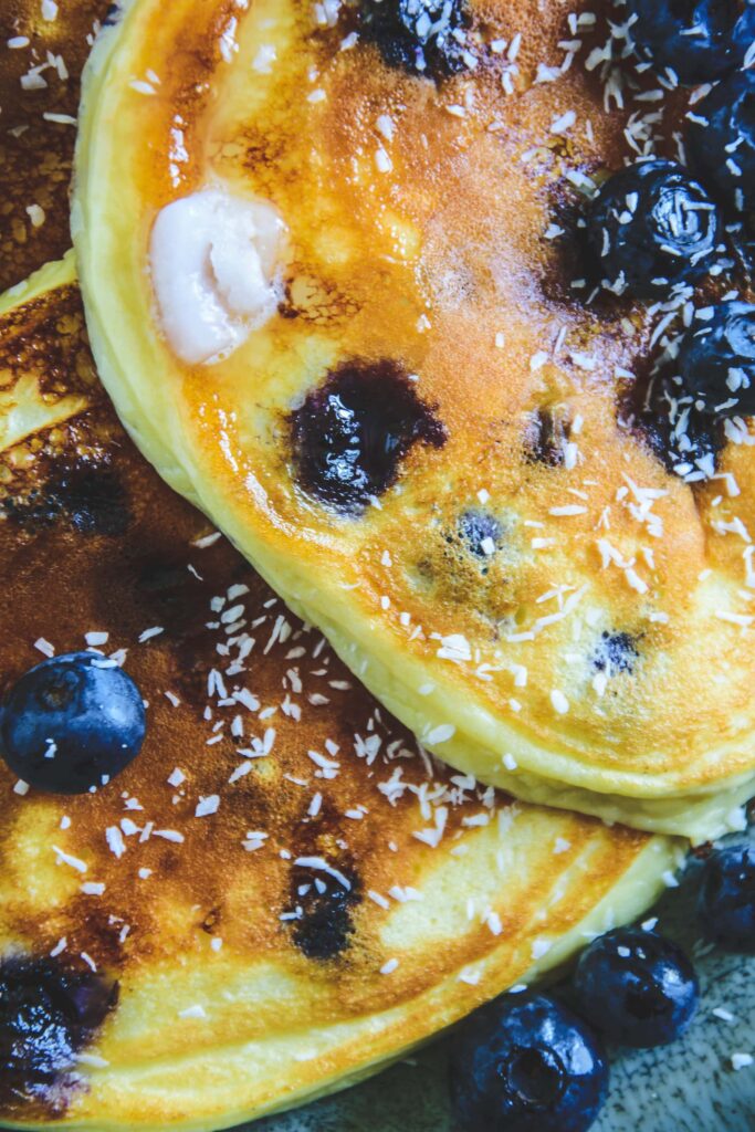 Heidelbeer-Topfen-Pancakes mit Gabel auf dunkeltürkisem Teller. Garniert mit Heidelbeeren. Top View.