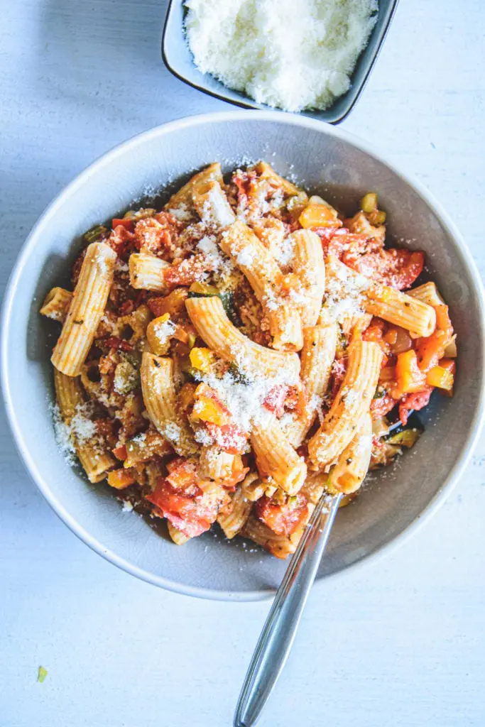 Gesunde Vollkornpasta mit Gemüsesugo in einem blauen Teller. Bestreut mit Parmesan. Löffel seitlich im Teller. Ansicht von oben.