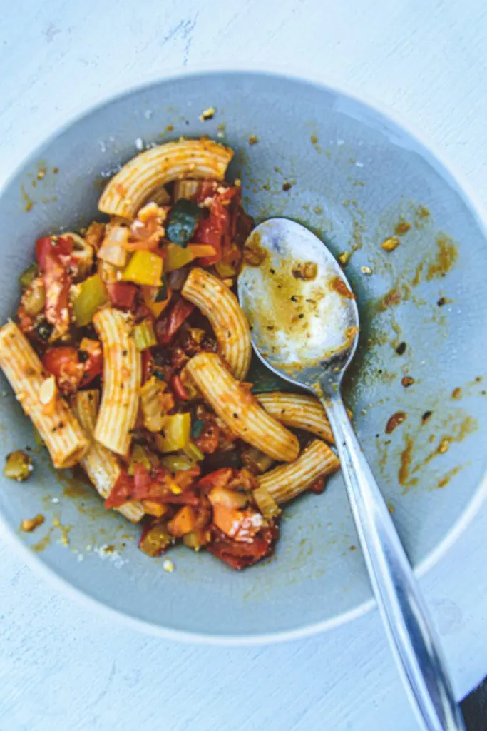 Halb leerer Teller Pasta mit Gemüsesugo von oben fotografiert.