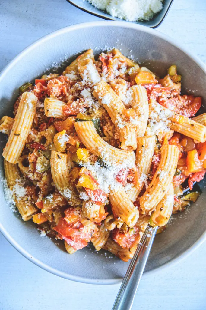 Gesunde Vollkornpasta mit Gemüsesugo in einem blauen Teller. Bestreut mit Parmesan. Löffel seitlich im Teller. Ansicht von oben.