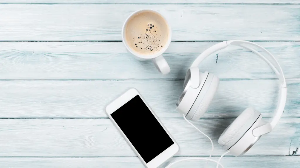 Flatlay auf hellblauem Holzuntergrund: weiße Kopfhörer, iPhone und Espresso