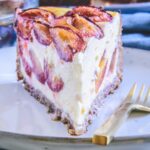 Ein Stück gesunder Zwetschgenkuchen mit Topfen und Nüssen im 45-Grad-Winkel auf einem grau-blauen, hellen Teller mit einer goldenen Gabel daneben.