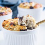 Banane-Schoko-Protein-Tassenkuchen in einer weißen kleinen Souffléform im 45-Grad-Winkel aufgenommen. Ein goldener Löffel hebt ein sehr saftiges Stück Kuchen aus der Form heraus.