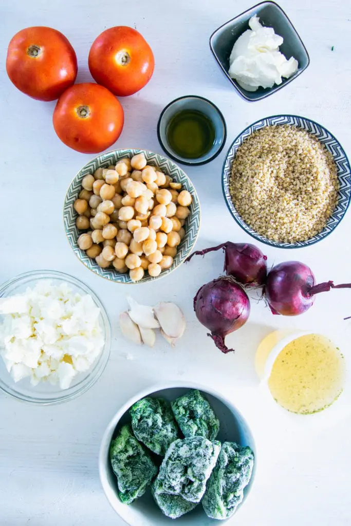 Zutaten für Bulgur-Spinatauflauf mit Kichererbsen, Tomaten und Feta auf weißem Untergrund. Flatlay.