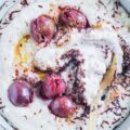 Dinkel-Grießbrei mit Schokolade und Kirschen in einer grauen Schüssel mit einem goldenen Löffel. Nahaufnahme von oben mit vielen Details. Der Löffel hat den Brei leicht vermischt.