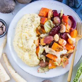 Herbst-Ofengemüse mit Polenta auf einem graublauen Teller mit goldener Gabel. Aufnahme von oben.