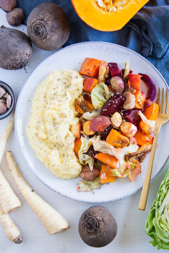 Herbst-Ofengemüse mit Polenta auf einem graublauen Teller mit goldener Gabel. Aufnahme von oben.