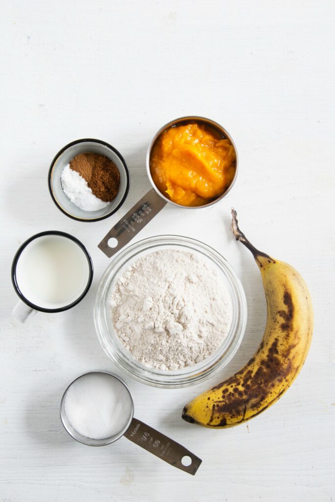 Zutaten für vegane Kürbis-Pancakes in Schüsseln auf weißem Untergrund. Flatlay.