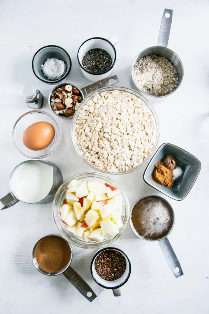 Zutaten für Oatmeal Muffins mit Apfel und Nüssen in Schüsseln und Cups. Flatlay auf weißem Untergrund.