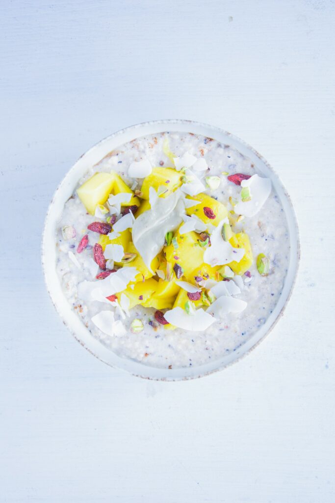 Porridge getoppt mit Mangeowürfeln, Gojibeeren, Kokoschips, Pistazien, Hanfsamen und Cashewmus. Aufnahme von oben.