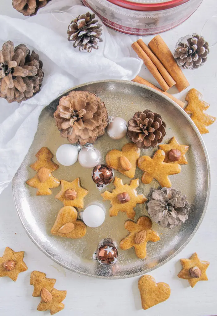 Gesündere Lebkuchen auf einem goldenen Teller, dekoriert mit kleinen Christbaumkugeln und Zapfen. Aufnahme von oben.