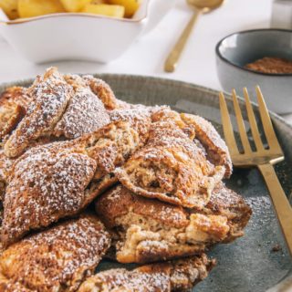 Lebkuchen-Schmarrn auf einem graugrünen Teller mit goldener Gaben. Aufnahme im 45-Grad-Winkel. Bratapfel-Orangenkompott im Hintergrund.