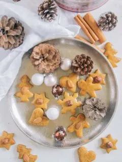 Gesündere Lebkuchen auf einem goldenen Teller, dekoriert mit kleinen Christbaumkugeln und Zapfen. Aufnahme von oben.