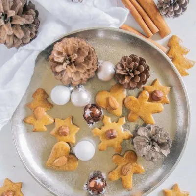 Gesündere Lebkuchen auf einem goldenen Teller, dekoriert mit kleinen Christbaumkugeln und Zapfen. Aufnahme von oben.