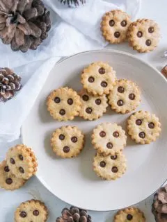 Linzer Augen auf einem hellbeigen Teller mit einem weißen Tuch und Zapfen als Dekoration. Aufnahme von oben